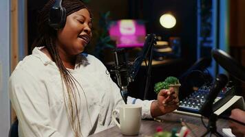 africano americano donna fare Podcast nel appartamento studio, indossare cuffie e parlando su professionale mic con ospite. vicino su tiro di bipoc influencer intervistando celebrità video