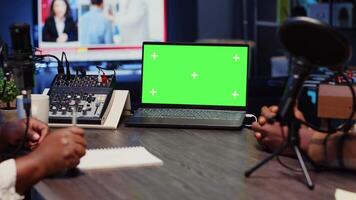 Green screen laptop next to cohosts streaming podcast using professional vlogging gadgets on vlog channel, panning shot. Mockup notebook between podcasters meeting in studio to film show, close up video