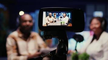 Focus on vlogging camera used by cohosts in blurry background streaming podcast during live debate on vlog channel. Close up of professional recording gear used by man and woman in studio to film show video