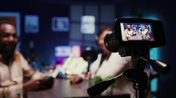 Focus on camera recording man on podcast in blurry background talking with guest during marathon stream for humanitarian cause. Close up of professional gear filming host during internet show video