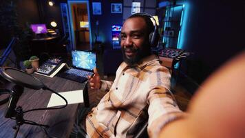 Journalist records interview with smartphone selfie camera in studio, reviewing notes to ask quality questions to guest. POV shot of BIPOC man using phone to film vlog, talking on mic with woman video