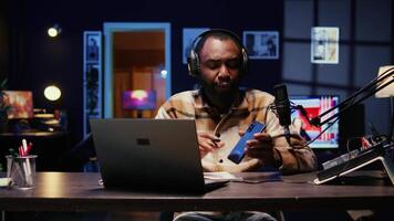 Portrait of african american tech expert reviewing newly released smartphone in rgb lights living room studio. Entertaining influencer filming technology channel vlog using professional camera video