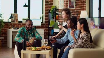 multirracial grupo de amigos hablando con cada otro en elegante departamento, reunido juntos a celebrar día festivo. multiétnico colegas socializando a hogar, disfrutando alcohólico bebidas video