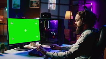 Man having fun by using green screen computer monitor to play singleplayer videogame. Professional gamer using mockup PC desktop to complete levels in game, talking with friends video