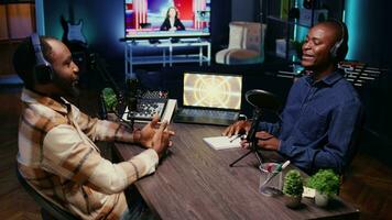 afrikanisch amerikanisch Influencer Aufzeichnung Podcast mit Gast, mit Audio- Aufzeichnung Ausrüstung im Zuhause Studio. heiter Männer chatten Leben während Rundfunk- Session zum Internet Show video