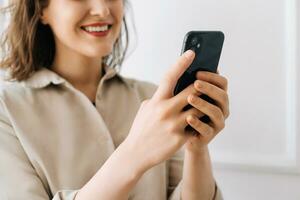 Smiling young woman typing on smartphone, chatting in social network, watch video. Digital Interaction Delight. Young Woman Smiles, Engaged in Smartphone Activities. Multitasking Maven photo