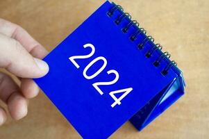 Hand showing year 2024 table calendar on wooden background. Calendar new year concept. photo