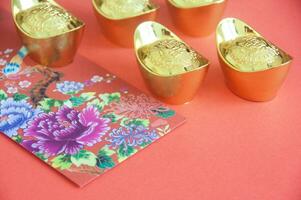 Chinese New Year decoration with colorful packets and golden ingots on red cover background photo