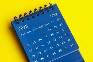 May 2025 blue desk calendar on yellow cover background. photo