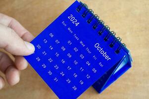 Hand showing October 2024 table calendar on wooden background. Calendar and new month concept. photo