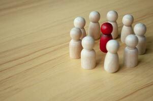 Red wooden doll surrounded by other dolls. Representing either discussion, leadership or harassment photo