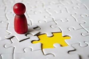 Red wooden doll on top of jigsaw with missing jigsaw puzzle. Hiring and employment concept photo
