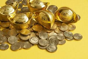 Close up view of golden ingot and coins on yellow cover background photo