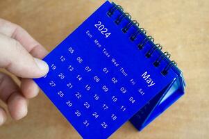 Hand showing May 2024 table calendar on wooden background. Calendar and new month concept. photo