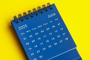 June 2025 blue desk calendar on yellow cover background. photo