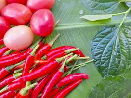 Picture of tomatoes and chili peppers placed on banana leaves. photo