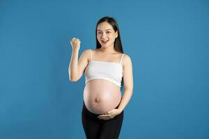 retrato de embarazada asiático mujer, aislado en azul antecedentes foto