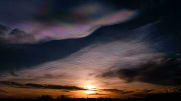 hermosa iridiscente sombrerillo nube terminado puesta de sol, rara natural de puesta de sol cielo de fuego arcoiris o arco iris nubes.oscuras nube con vistoso óptico fenómeno cielo en invierno noche en Reino Unido foto