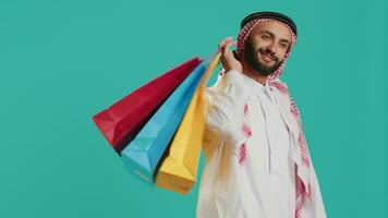 Young adult carrying shopping bags on camera, feeling pleased after successfully buying products and merchandise. Middle eastern guy purchasing things on sale at mall store, retail paper bags. video