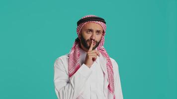 Arabic adult showing silence symbol with finger over lips, presenting hush mute sign on camera. Private person doing confidential secrecy gesture in studio, trying to keep secret. video