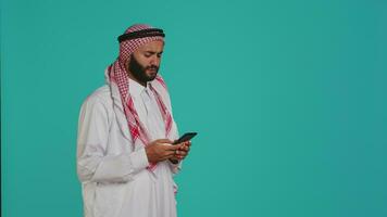 muslim modell svar mobil telefon ring upp på trådlös enhet, kommunicerar på avlägsen telefon linje. ung person representerar islamic tradition med kostym och huvudduk, svar chatt. video