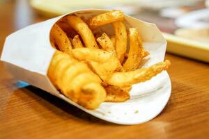 Spiral french fries in white box and on wooden table and blurry background. photo