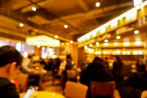 borroso de pueblos y turistas en un moderno restaurante con amarillo calentar luces. foto