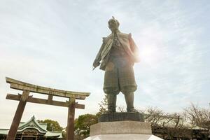 osaka, Japón, junio 20 2018 - de cerca toyotomi hideyoshi estatua ciudad regla de Osaka ciudad y propietario de Osaka castillo., nacido en ad1583 en el Osaka castillo parque zona y de madera torii portón en azul cielo. foto