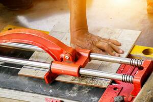 Closeup hands of laborer using cutting tile machine at construction site with sun flare background. photo