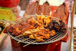 Closeup barbecue seafood with wood stick on grill and stove sell in Kuromon street martket. One of tourist popular snack food at Kuromon market ,Osaka city, Japan photo