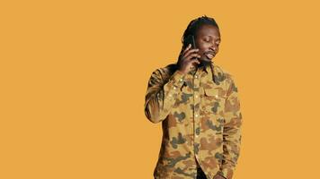 Young adult chatting on phone call in studio, talking to people on remote telephone line over orange background. African american person having fun with telecommunication conversation. video