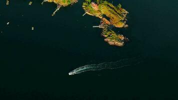 Top down view of motor boat sails around the coast of the island. Camera rotates video