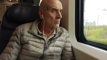 antiguo hombre con auriculares mirando fuera el ventana admirativo el ciudad por tren video