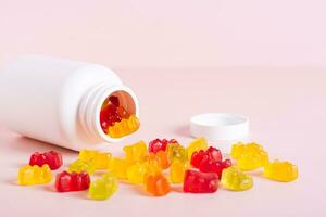 Chewable vitamin supplements spilled from a bottle on a pink background photo