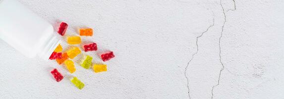 Bottle with gummy vitamin supplements in the shape of bears on the table top view web banner photo