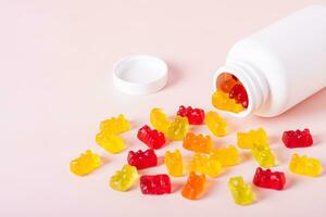 Group of gummy supplements with multivitamins and a bottle for them on a pink background photo