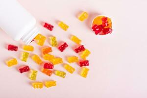Chewable vitamin supplements spilled from a bottle on a pink background top view photo