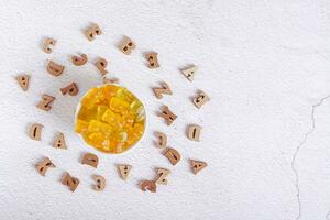 Chewable multivitamins in the form of candy bears in a bowl and wooden letters top view photo