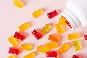 Group of gummy supplements with multivitamins and a bottle for them on a pink top view photo