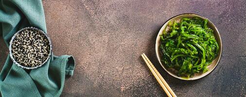 Delicious wakame seaweed salad on a plate and sesame seeds in a bowl top view web banner photo
