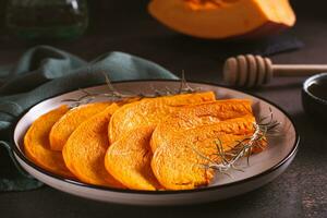 Homemade baked pumpkin pieces with rosemary on a plate on the table photo
