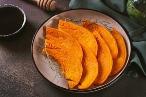 Seasonal vegetarian dish sliced baked pumpkin with herbs on a plate on the table photo