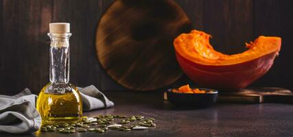 Fresh pumpkin seed oil and pumpkin pieces on the table web banner photo