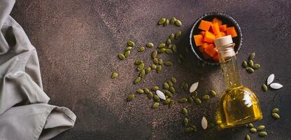 Organic vegetable oil from pumpkin seeds and pieces of pumpkin on the table top view web banner photo