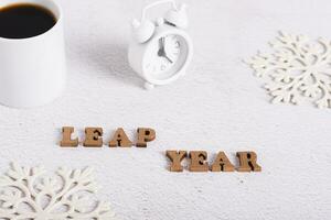 Leap year concept, text from wooden letters, alarm clock, coffee and snowflakes on light photo