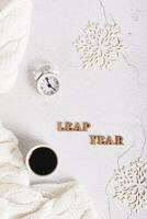 Leap year concept, coffee, alarm clock, snowflakes and letters on a light top and vertical view photo