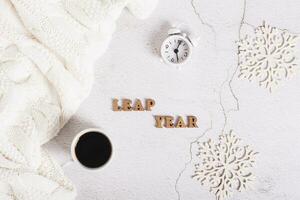 Leap year concept, coffee, alarm clock, snowflakes and letters on a light background top view photo