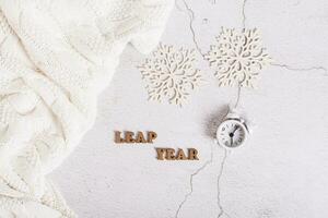 Leap year concept, calendar, alarm clock, sweater and snowflakes on a light top view photo