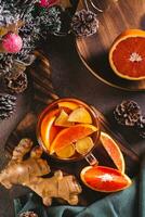 Delicious homemade tea with orange and ginger in a glass mug on the table top and vertical view photo