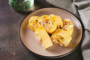 Mini tortilla rolls with chopped sausages, cheese, eggs and herbs on a plate on the table photo